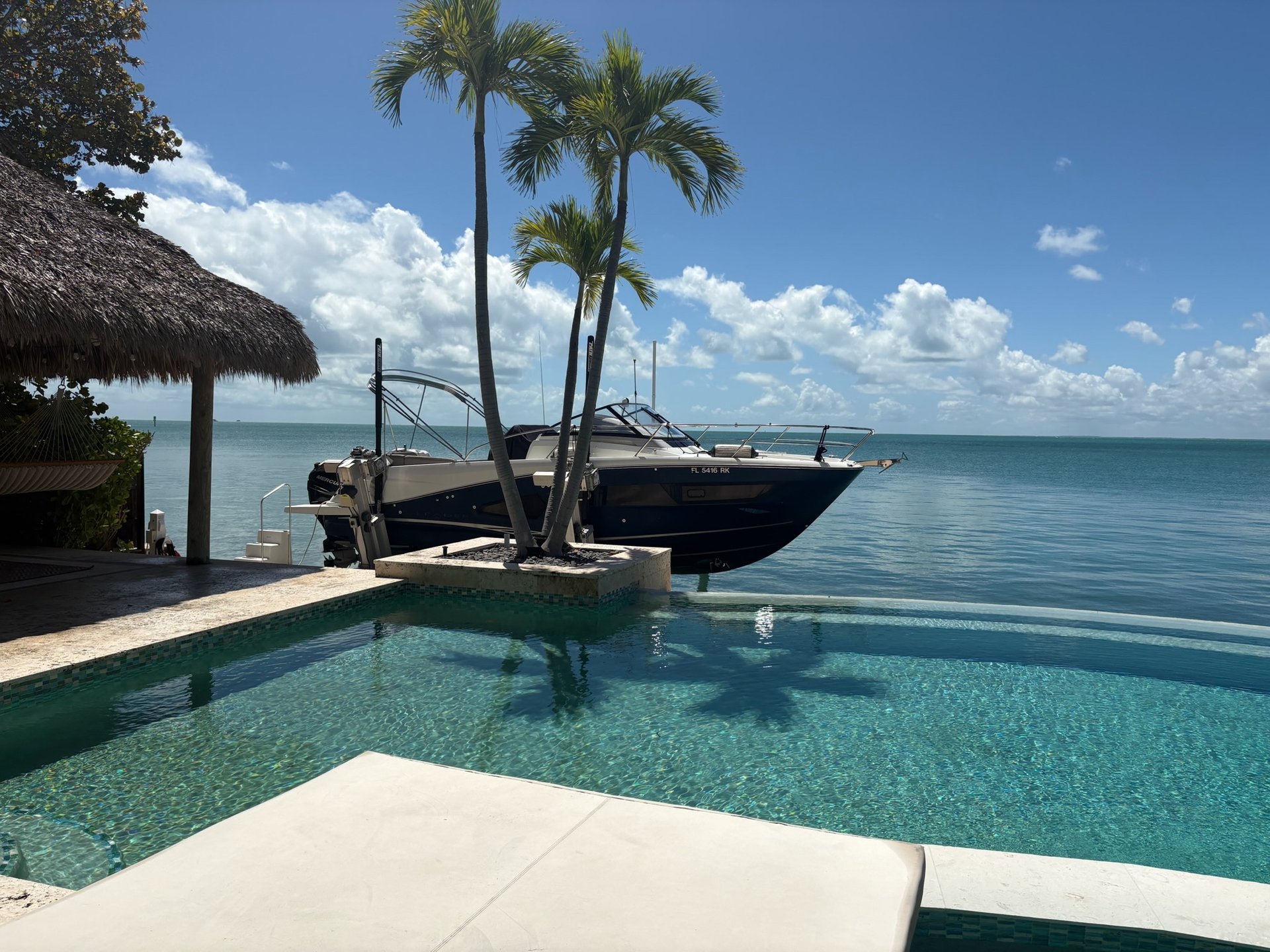 Luxury waterfront boat lift installation with cruiser, infinity pool, and Florida palm trees